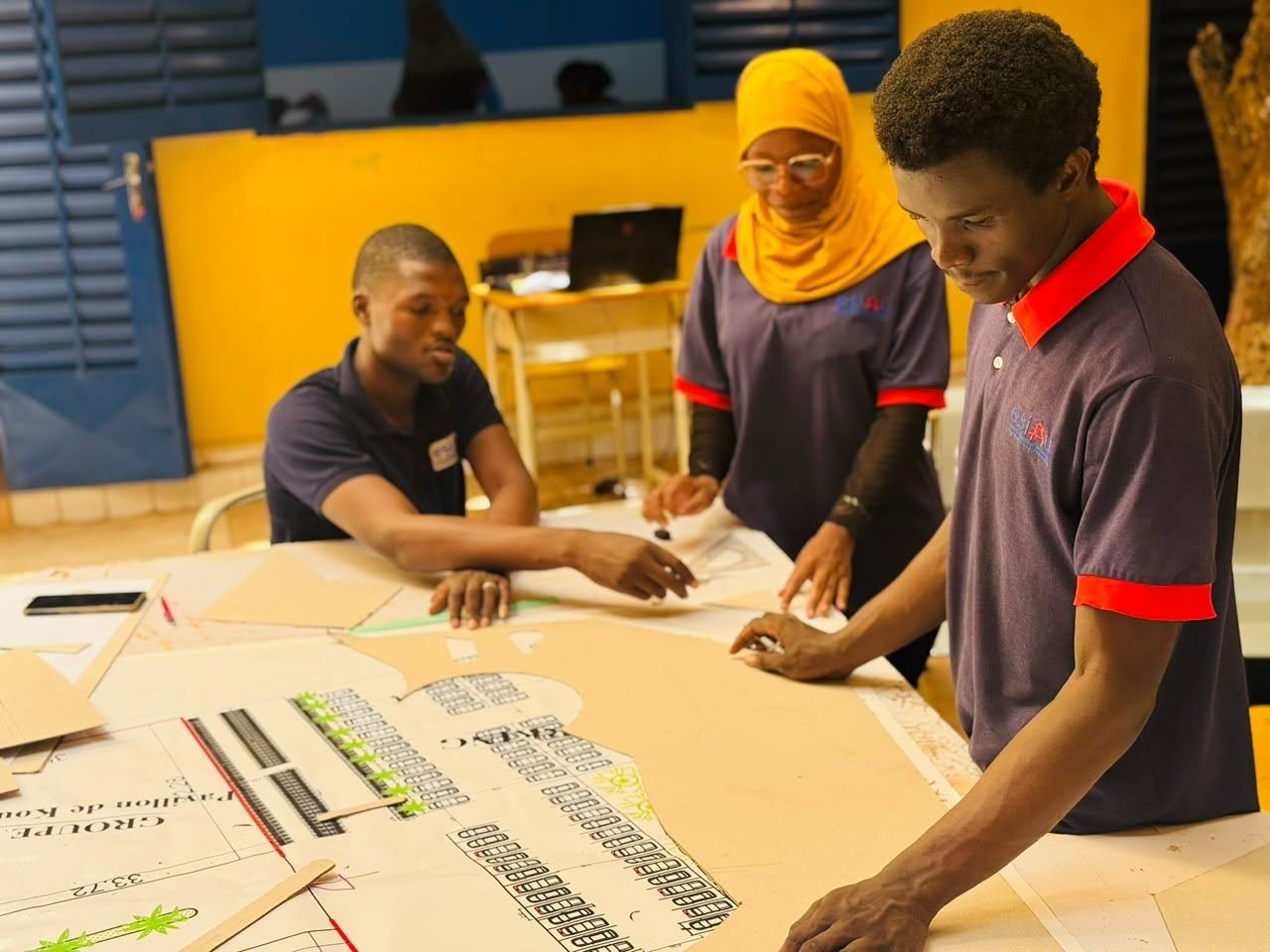 Trois étudiants en polo ESIAU travaillent ensemble autour d'un grand plan posé sur une table d'atelier
